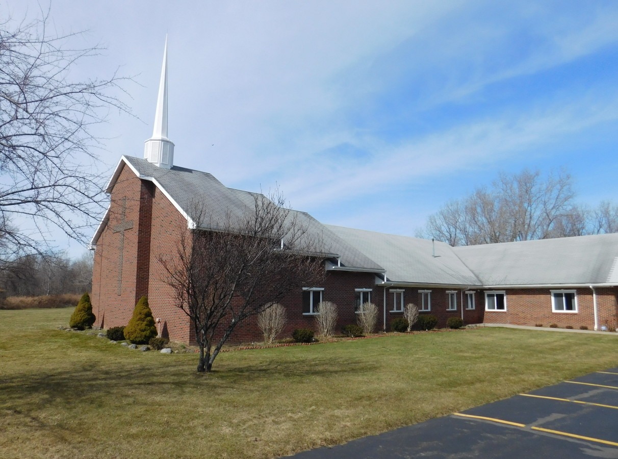 A brown-bricked church with a grey roof and tall white steeple