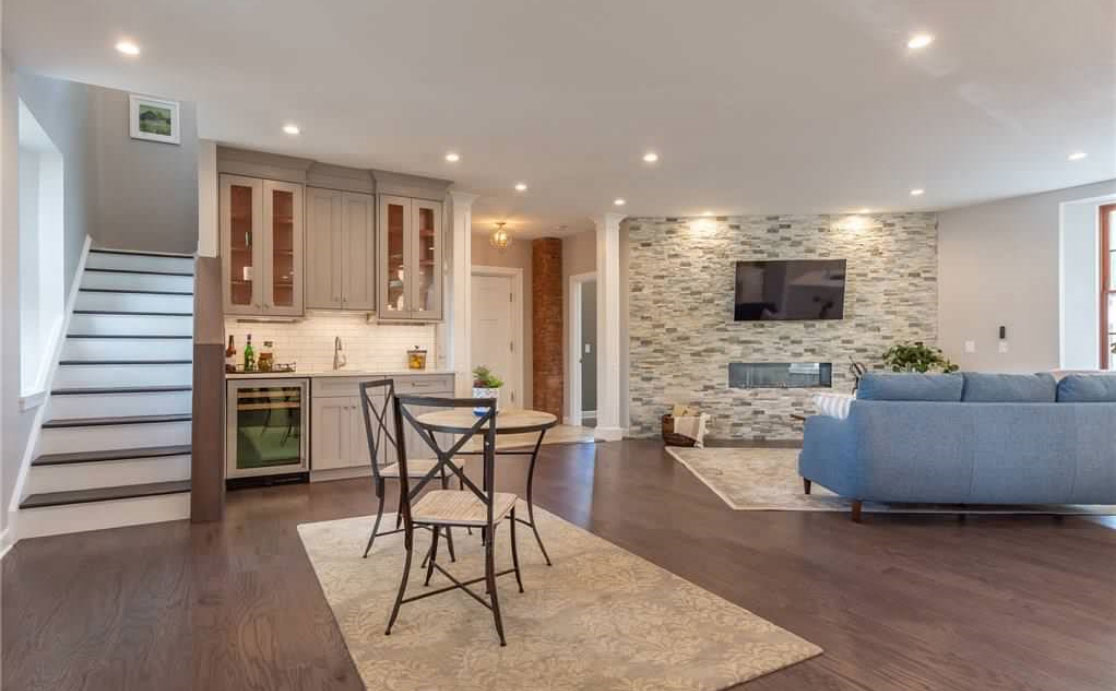 A large, open basement with wood flooring, a minibar, and couch with TV